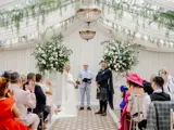 Bride and groom standing with the officiant during a wedding ceremony inside the Pavilion at Cornhill Castle in Biggar, Scotland, decorated with cascading greenery, chandeliers, and large white floral arrangements