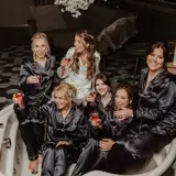 bride and bridesmaids sitting on couch drinking for photoshoot