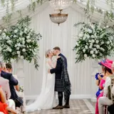 A wedding ceremony taking place at the Pavilion at Cornhill Castle in Biggar, Scotland, featuring an elegant setup with floral decorations and guests in attendance.