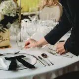 Person setting up elegant glassware on a white table set up at Grand Ballroom at Boclair House, Glasgow