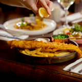 Freshly served fish and chips with lemon being squeezed over the crispy batter at the Plumpy Duck, hotel restaurant at Bowfield Hotel & Spa, a spa hotel near Glasgow.