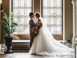 bride and groom standing inside ornate hall by window