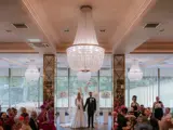 A couple standing at altar during elegant indoor ceremony at Boclair House, Bearsden, a Glasgow wedding venue with grand chandeliers, floral décor and guests either side of the aisle.