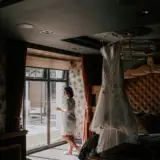 Wedding dress hanging in honeymoon suite with bride in background 